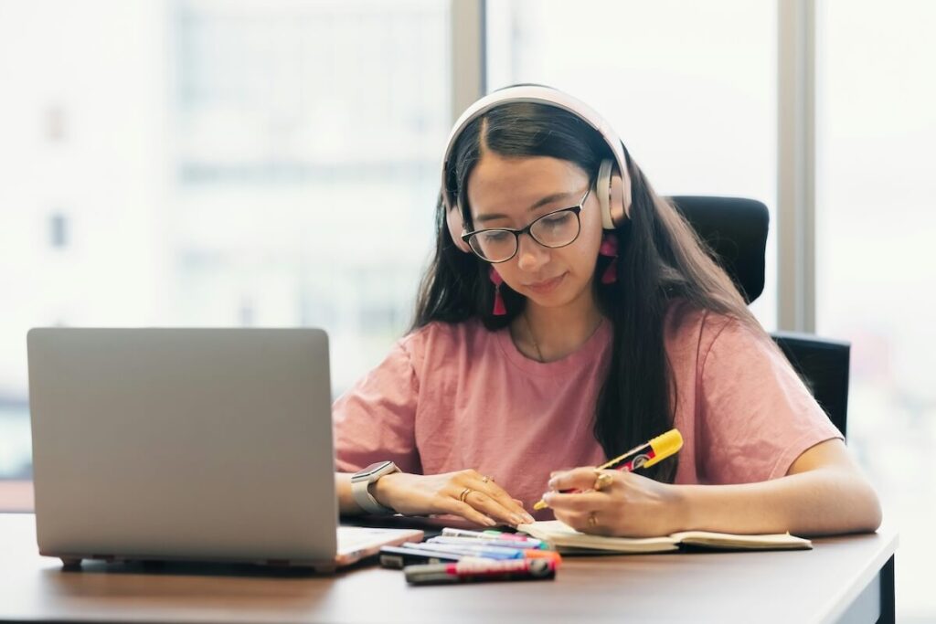 female student studying with laptop, notebook, and headphones